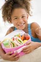 Young girl holding packed lunch in living room smiling