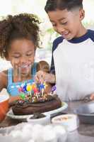 Two children in kitchen with birthday cake smiling