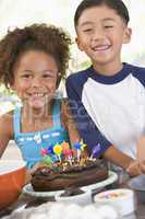 Two children in kitchen with birthday cake smiling