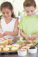 Two children in kitchen decorating cookies smiling