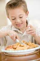 Young boy indoors eating fish and chips smiling