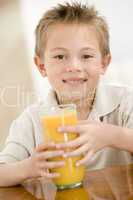 Young boy indoors with orange juice smiling