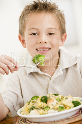 Young boy indoors eating pasta with brocolli smiling