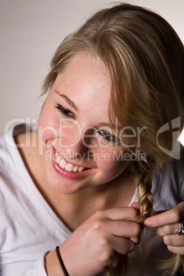 junge blonde lächelnde Frau flechtet sich Zopf