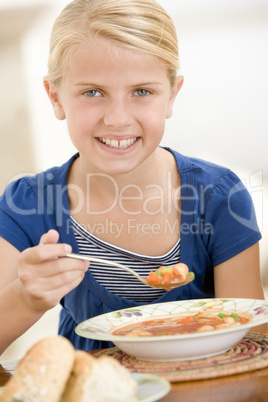 Young girl indoors eating soup smiling