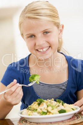 Young girl indoors eating pasta with brocolli smiling