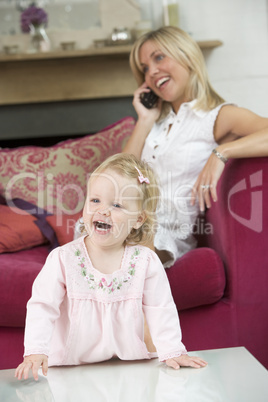 Mother using telephone in living room with baby smiling