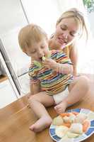 Mother and baby in kitchen eating fruit and vegetables