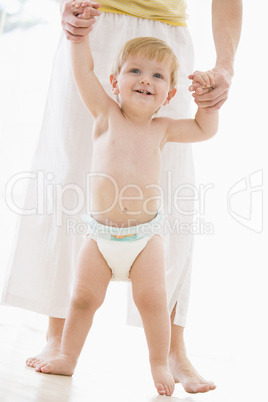 Mother helping baby walk indoors smiling