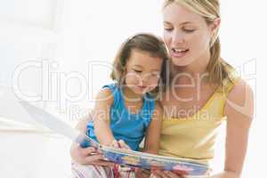 Mother and daughter indoors reading book and smiling