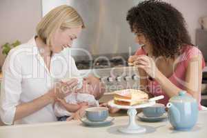 Mother and baby in kitchen with friend eating cake and smiling