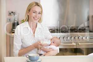 Mother feeding baby in kitchen with coffee smiling