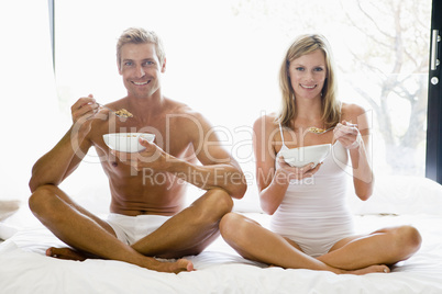 Couple sitting in bed eating cereal and smiling