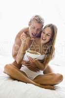 Couple sitting in bed eating cereal and smiling