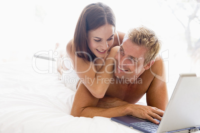 Couple lying in bed with laptop smiling