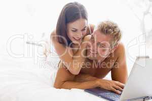 Couple lying in bed with laptop smiling