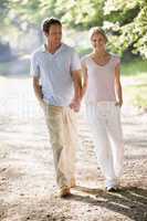 Couple walking outdoors holding hands and smiling