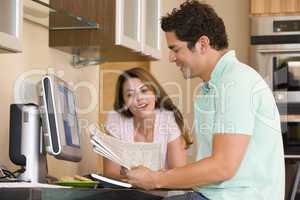 Couple in kitchen with computer and newspaper smiling