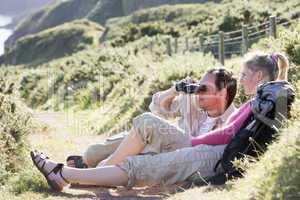 Couple on cliffside outdoors using binoculars and smiling