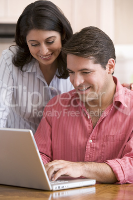 Couple in kitchen with paperwork using laptop smiling