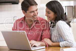 Couple in kitchen using laptop and smiling