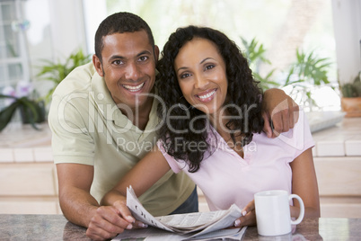 Couple in kitchen with newspaper and coffee smiling