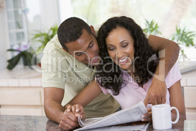 Couple in kitchen with newspaper and coffee smiling