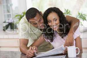 Couple in kitchen with newspaper and coffee smiling