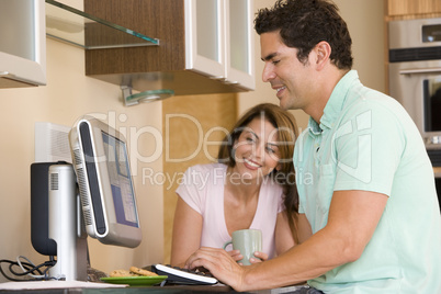 Couple in kitchen with computer and coffee smiling