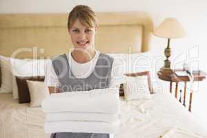 Maid holding towels in hotel room smiling