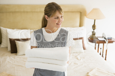 Maid holding towels in hotel room smiling