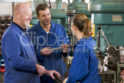 Three machinists in workspace by machine talking