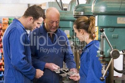 Three machinists in workspace by machine talking