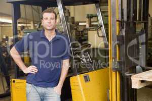 Warehouse worker standing by forklift