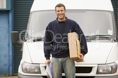 Delivery person standing with van holding clipboard and box smiling