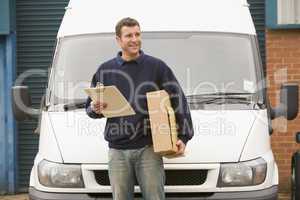 Delivery person standing with van holding clipboard and box smiling