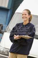 Delivery person standing with van writing in clipboard smiling