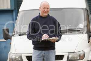 Delivery person standing with van writing in clipboard