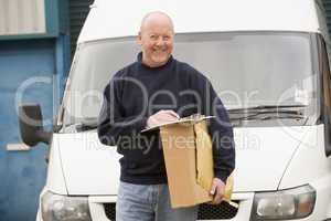 Delivery person standing with van with clipboard and box smiling