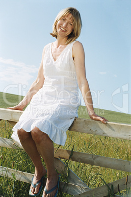 Woman sitting on fence outdoors smiling