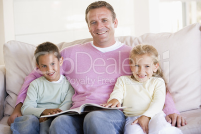 Man and two children sitting in living room reading book and smi