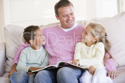 Man and two children sitting in living room reading book and smi