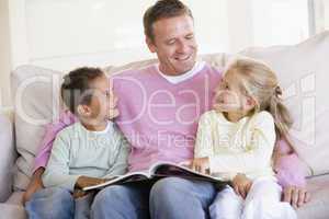 Man and two children sitting in living room reading book and smi