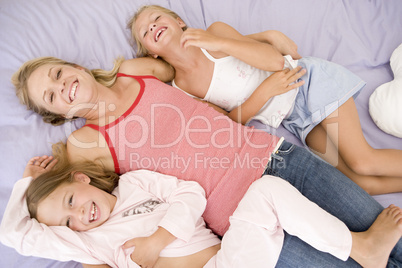 Woman and two young girls lying in bed playing and smiling