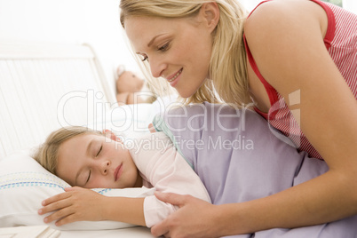 Woman waking young girl in bed smiling