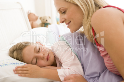 Woman waking young girl in bed smiling