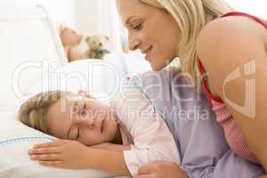 Woman waking young girl in bed smiling