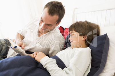 Man reading book to young boy in bed smiling