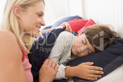 Woman waking young boy in bed smiling