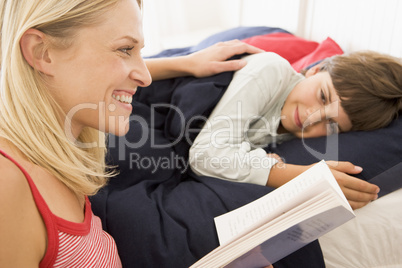 Woman reading book to young boy in bed smiling